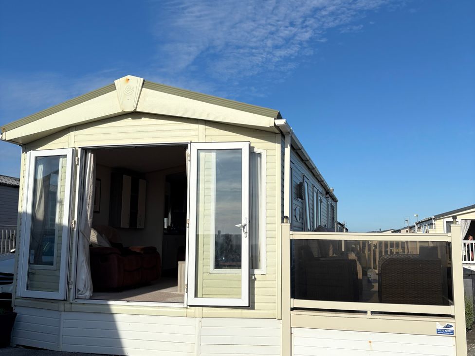 A caravan with open doors and decking area at Trecco Bay holiday park, Porthcawl