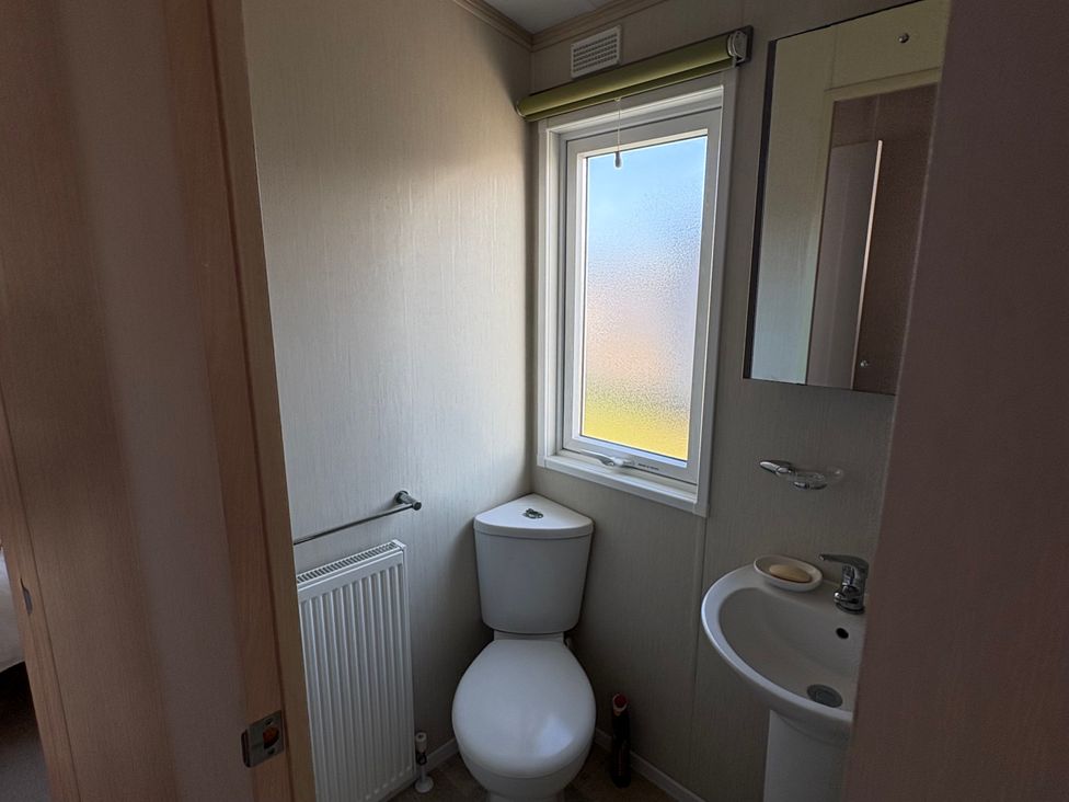 A bathroom with a toilet, sink, and window at Trecco Bay holiday park, Porthcawl