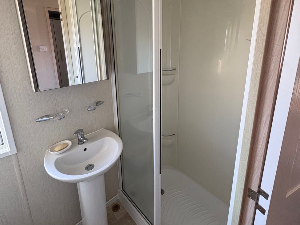 A bathroom featuring a sink, mirror, and shower cubicle at Trecco Bay holiday park, Porthcawl