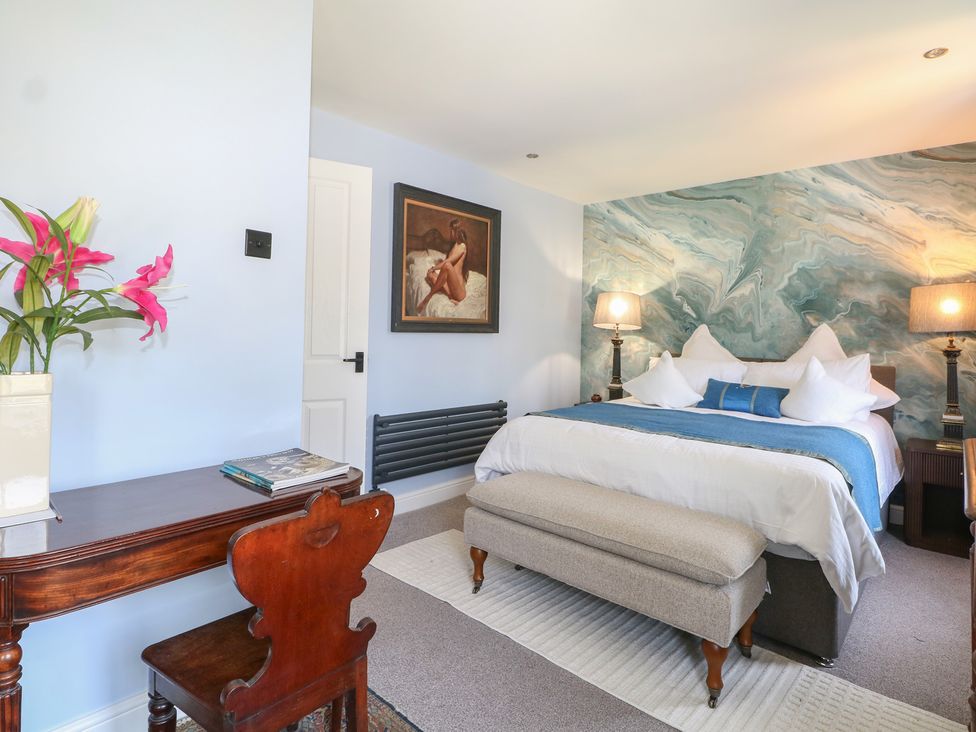 A bedroom featuring a bed, table, chair, and artwork at The Dacha in Winchester