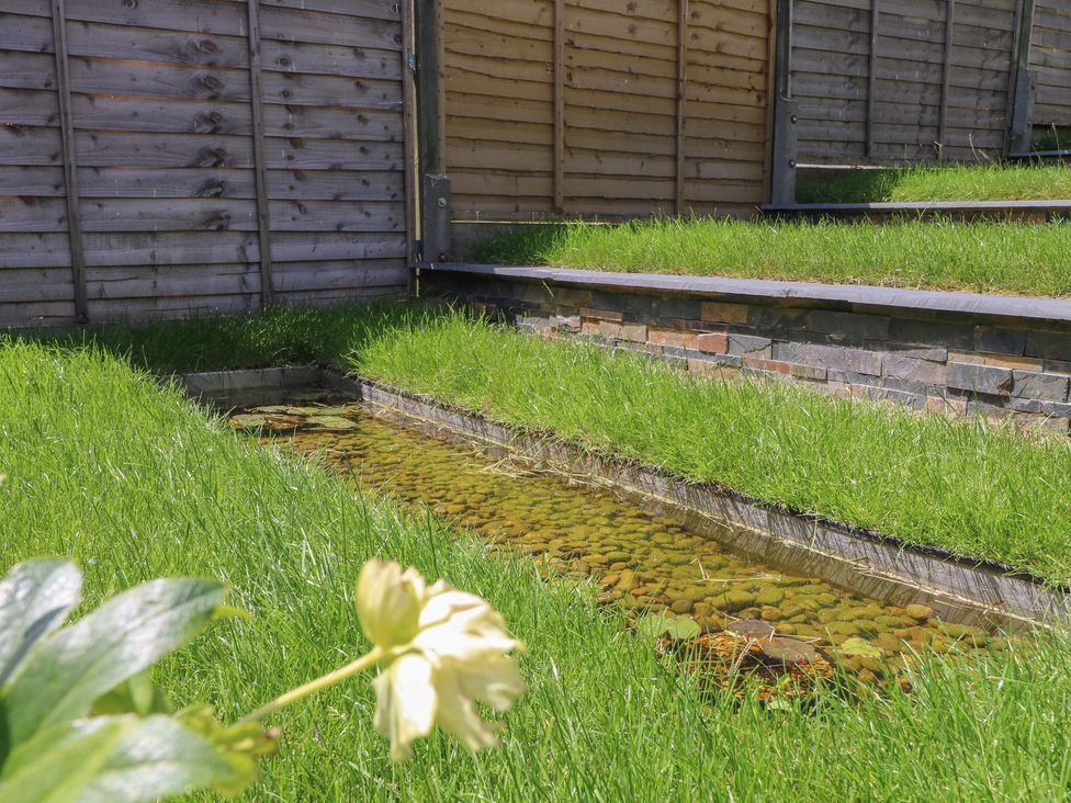 A garden with grass, a pond, and a stone wall at The Dacha in Winchester