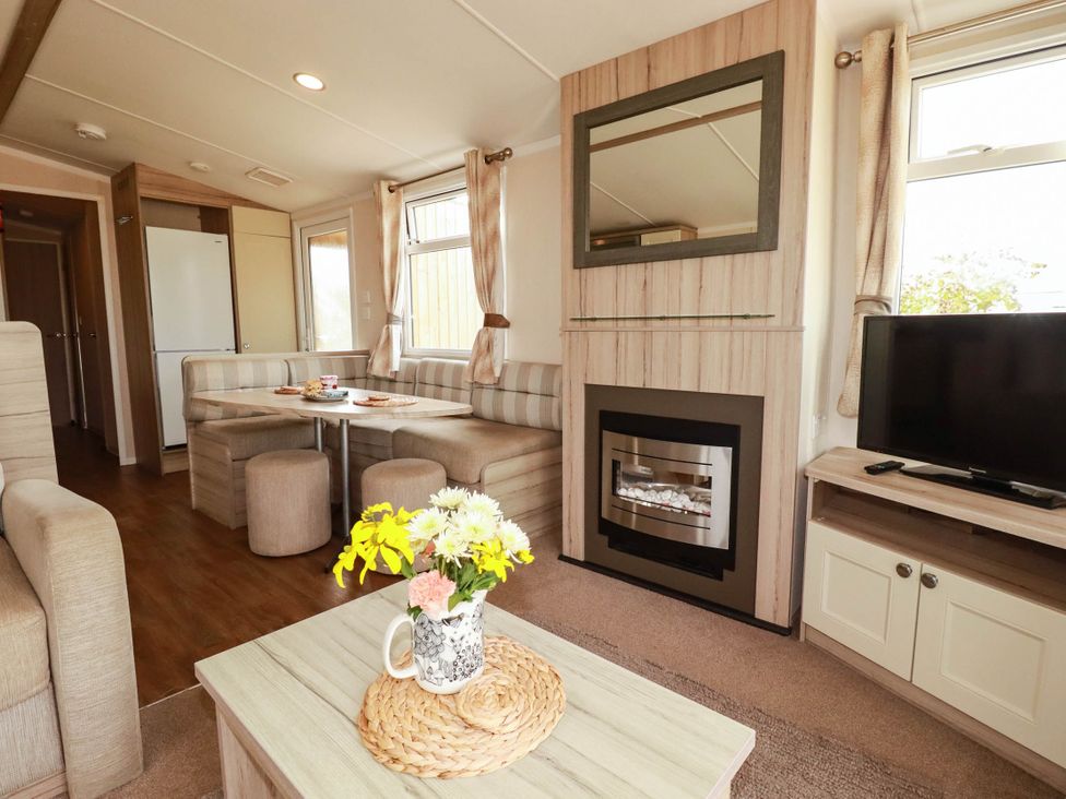 A living room with a table and chairs, television, and fireplace at Roslenn in St Agnes