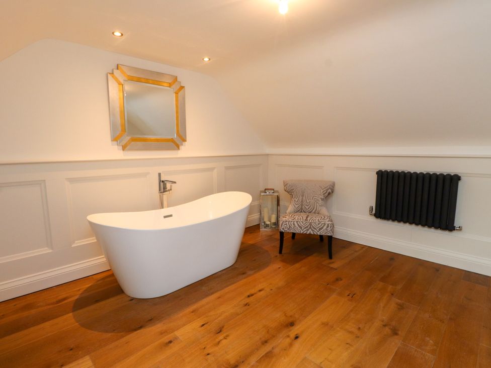 A bathroom with a bathtub, chair, mirror, and radiator at The Barn at Bryn Eithin in Colwyn Bay