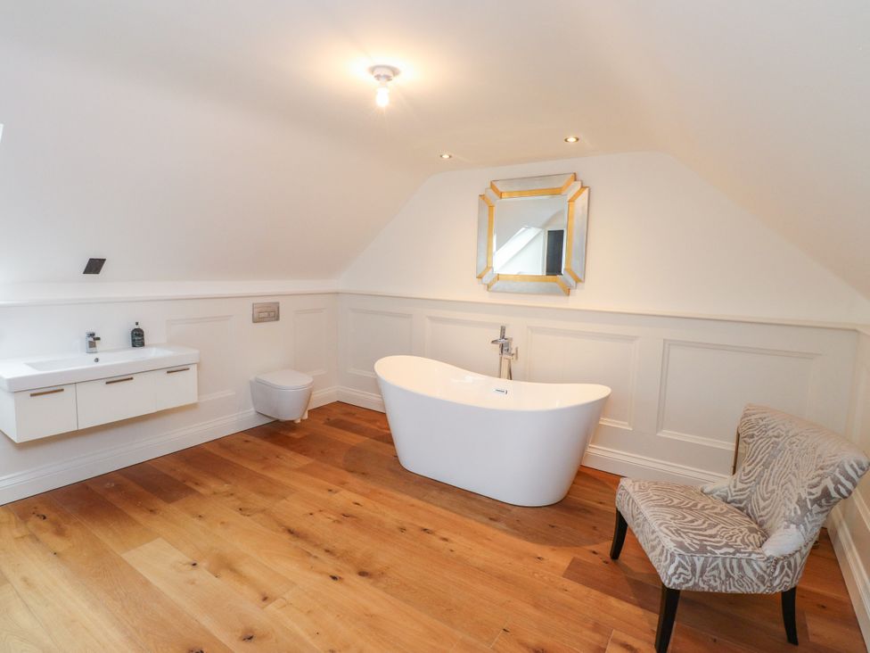 A bathroom featuring a bathtub, toilet, sink, and a chair at The Barn at Bryn Eithin in Colwyn Bay