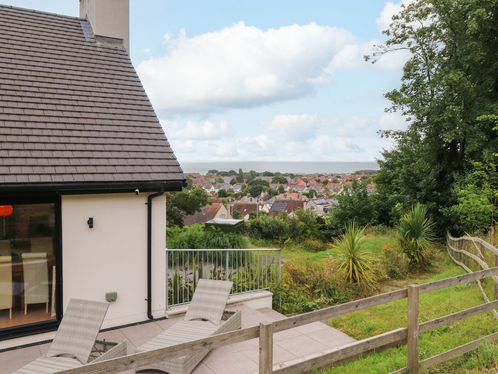 An outdoor area with a house and chairs overlooking the view at The Barn at Bryn Eithin Colwyn Bay