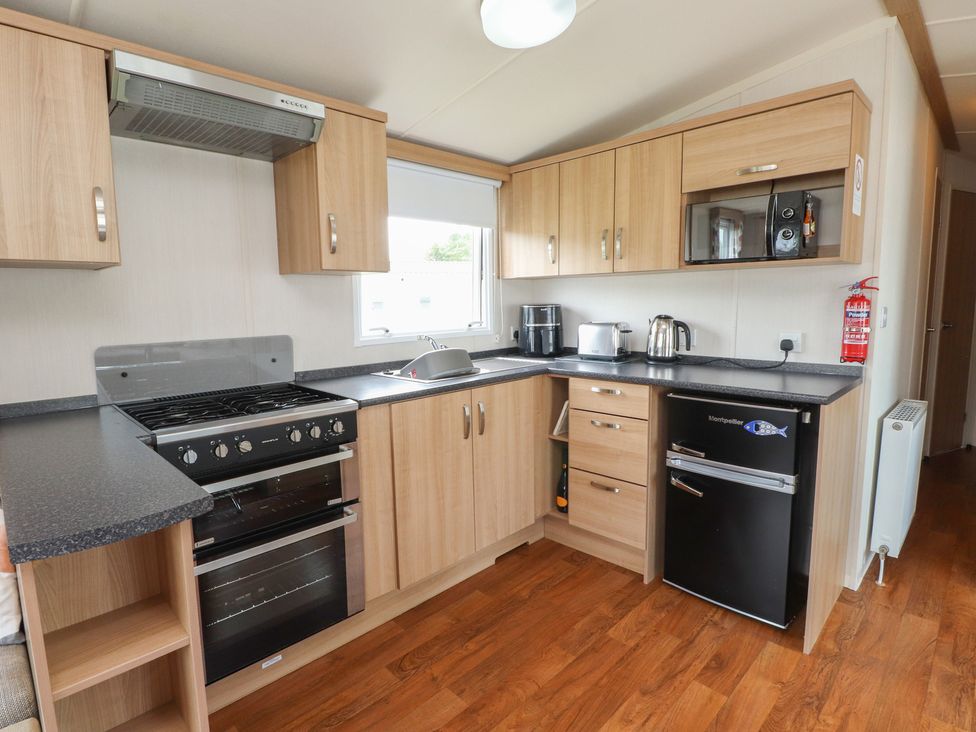 A kitchen with cabinets, oven, sink, kettle and fridge at 10 Cambrian Park Pwllheli