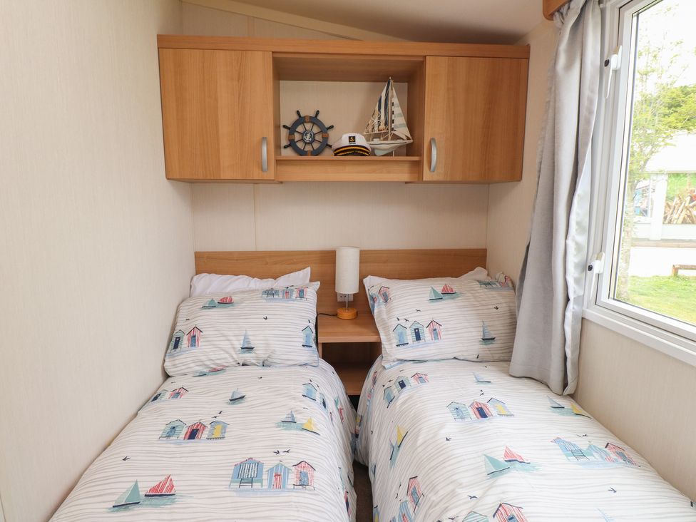A bedroom with two beds and a shelf at 10 Cambrian Park Pwllheli