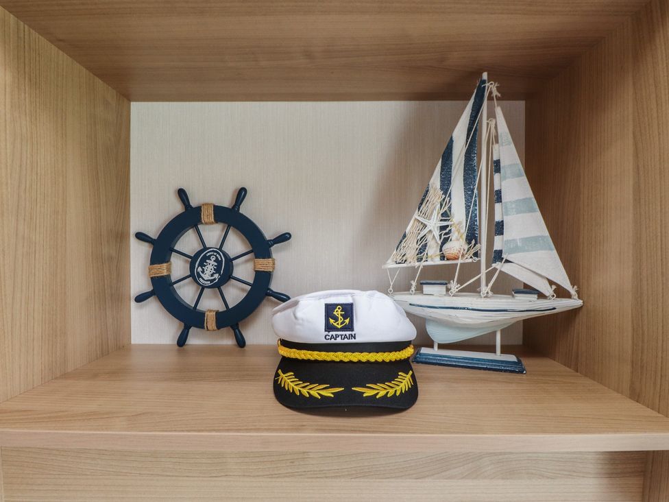 A shelf with a sailboat, captain hat, and ship wheel at 10 Cambrian Park, Pwllheli
