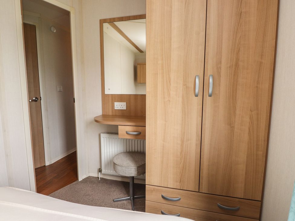 A bedroom featuring a wardrobe and desk with a mirror at 10 Cambrian Park in Pwllheli