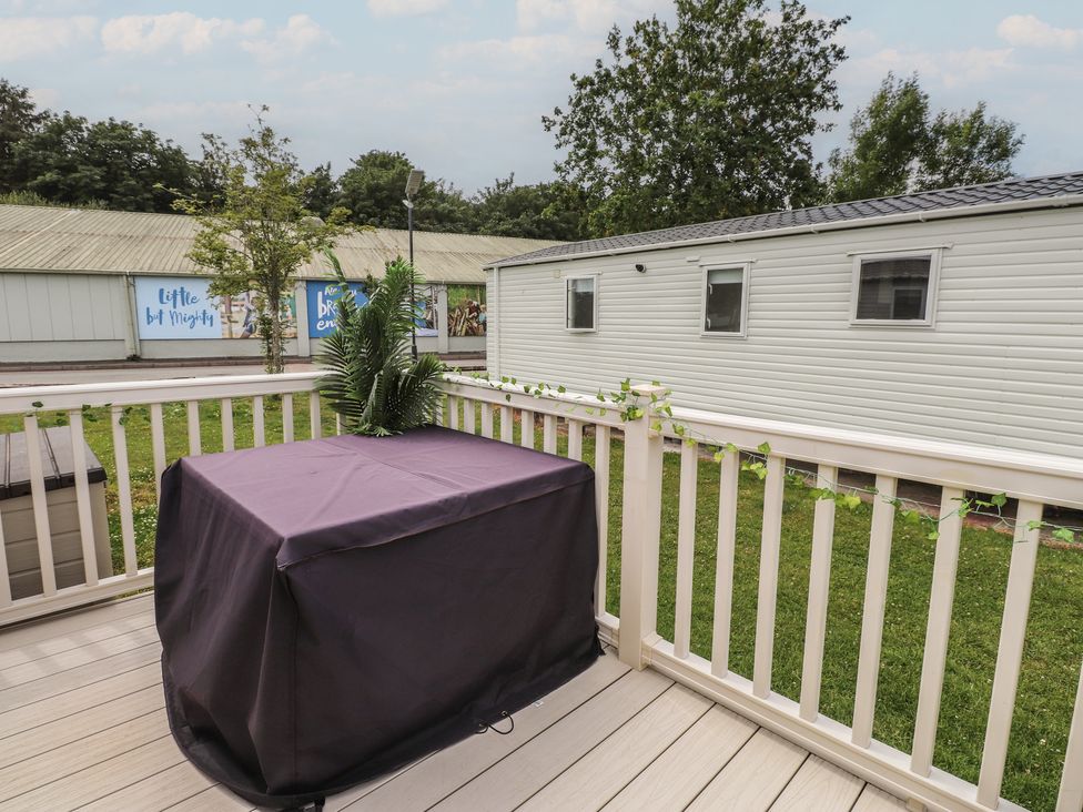 An outdoor deck with a table covered and a plant at 10 Cambrian Park Pwllheli