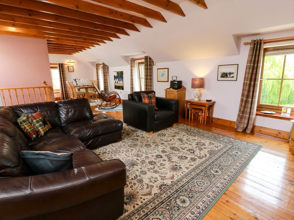 A living room with a sofa, armchair, table, and window at Buchanan’s Bothy Glencarse