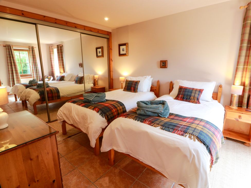 A bedroom with two beds, a mirror, dressers and window curtains at Buchanan’s Bothy in Glencarse