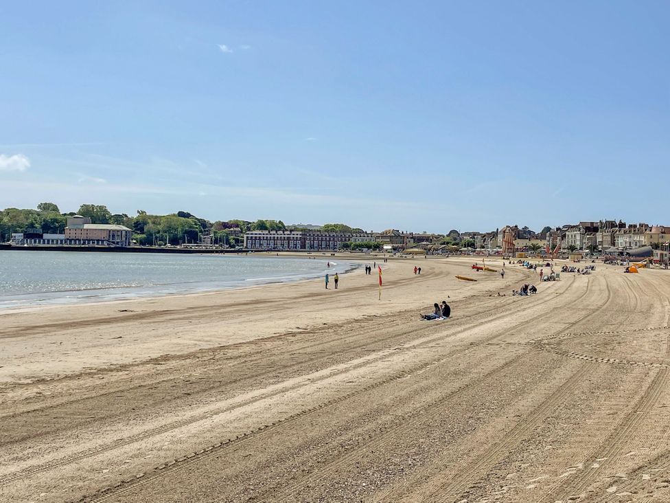 A beach with people walking and sitting at The Watch House in Weymouth
