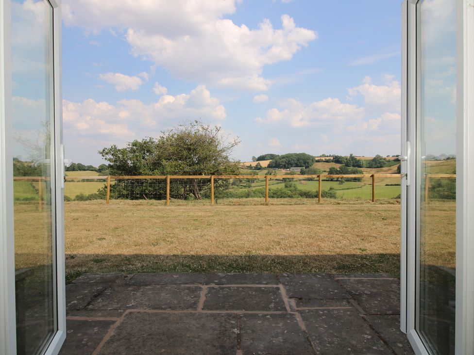 A view of a grassy field and trees from an open patio door at Wood Cottage in Tenbury Wells