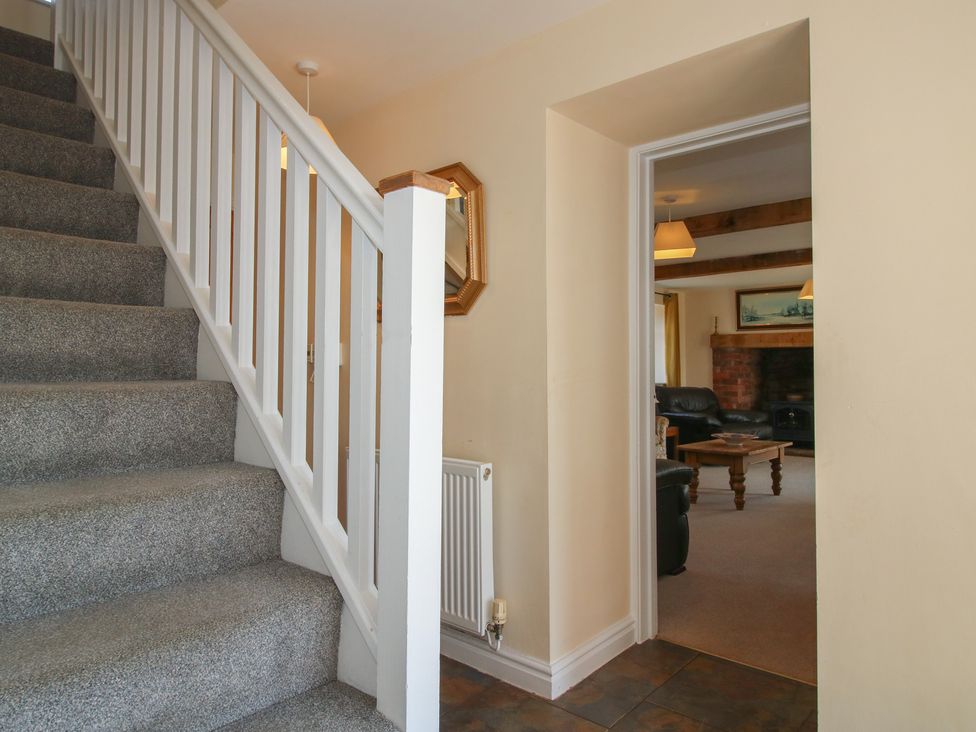 A hallway with a staircase and doorway leading to living area at Wood Cottage in Tenbury Wells