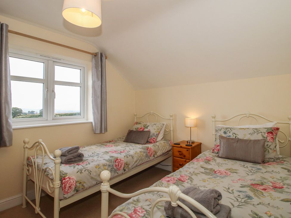 A bedroom with two beds, a lamp, and a window at Wood Cottage, Tenbury Wells