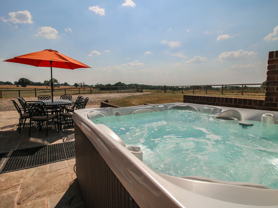 A hot tub and seating area with umbrella at Wood Cottage in Tenbury Wells