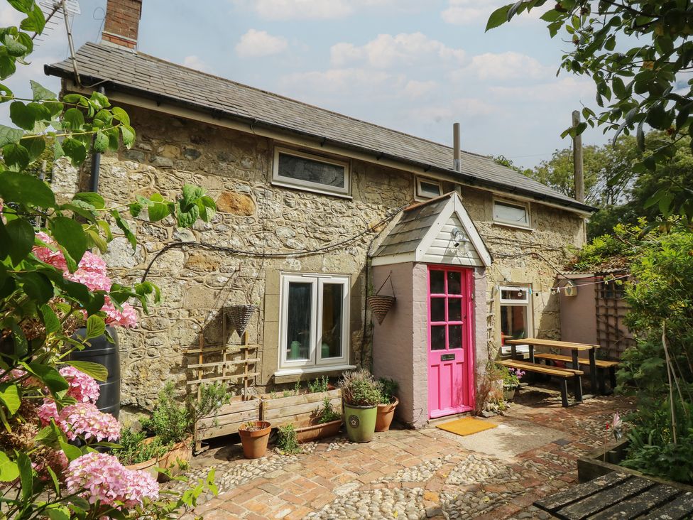 An outdoor area with a pink door and stone walls at Dairy Cottage in Whitwell near Niton