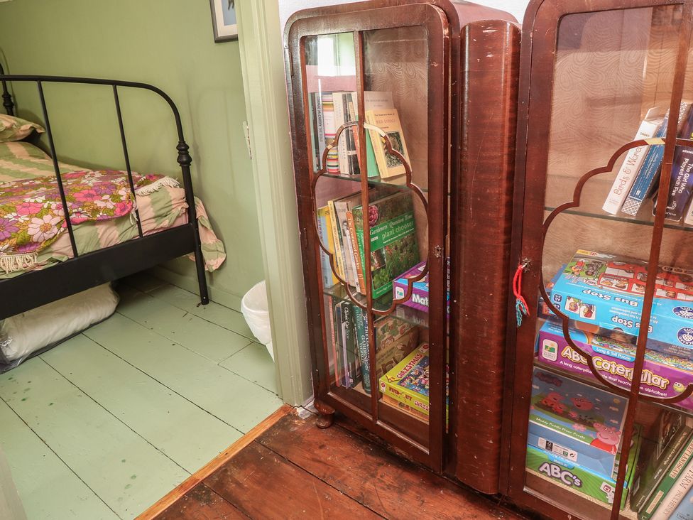 A bookshelf with games and books beside a bed at Dairy Cottage in Whitwell near Niton