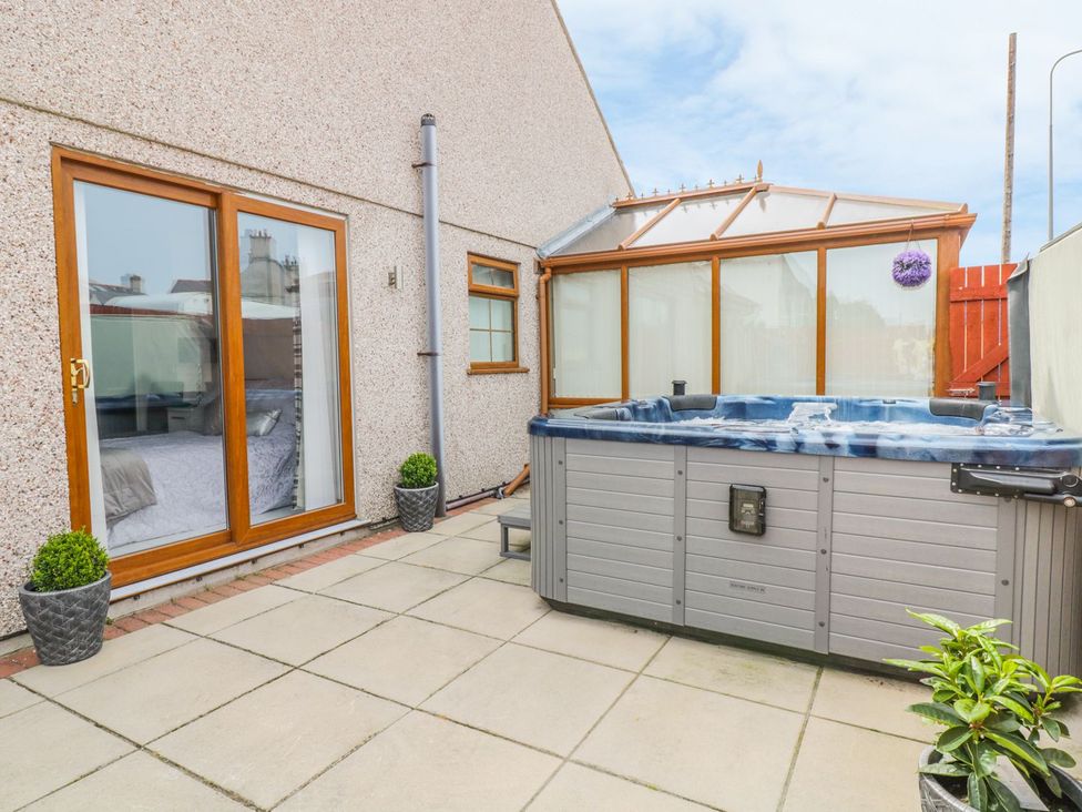 A patio area with a hot tub and sliding doors at Smithy Cottage in Cemaes Bay