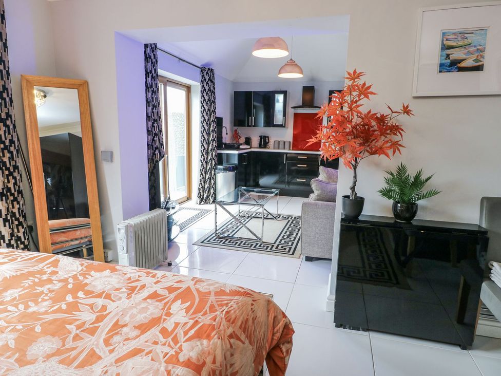 A living room with a mirror and kitchen area at Smithy Cottage in Cemaes Bay
