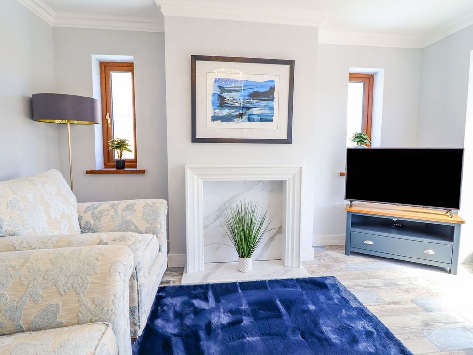A living room with a sofa, lamp, and television at Trefin Cemaes Bay