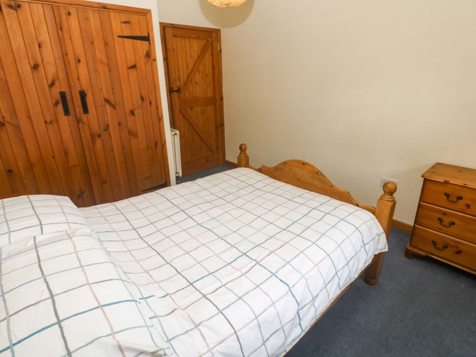 A bedroom with a wooden bed and wardrobe at Swallow Cottage Helston