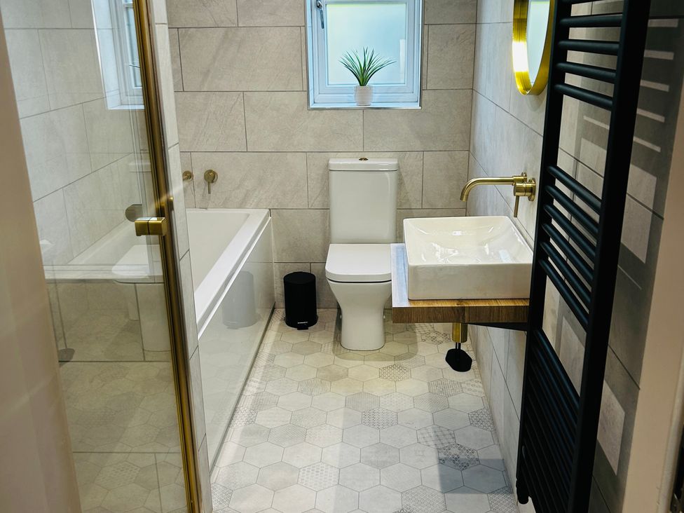 A bathroom with a tub, toilet, sink and window at Badger Cottage in Wold Newton