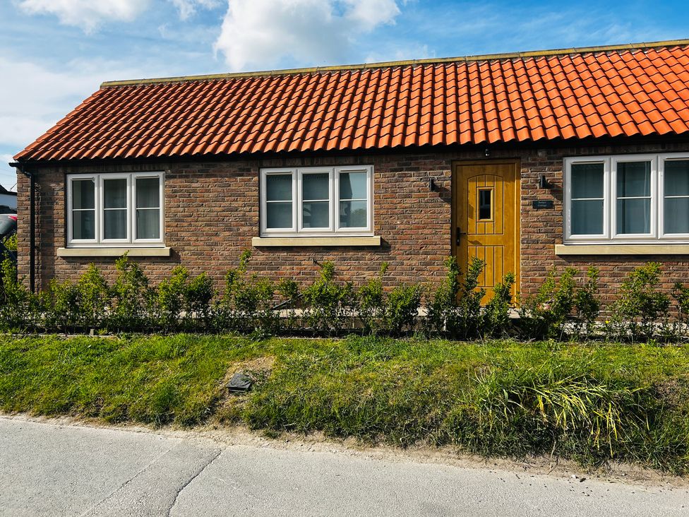 A house with a brick wall and a wooden door at Badger Cottage in Wold Newton