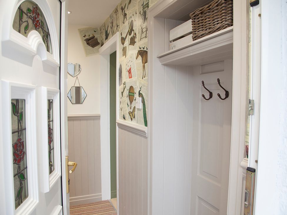 A hallway with a door, mirror, hooks, and storage basket at Snug Cottage in Honley