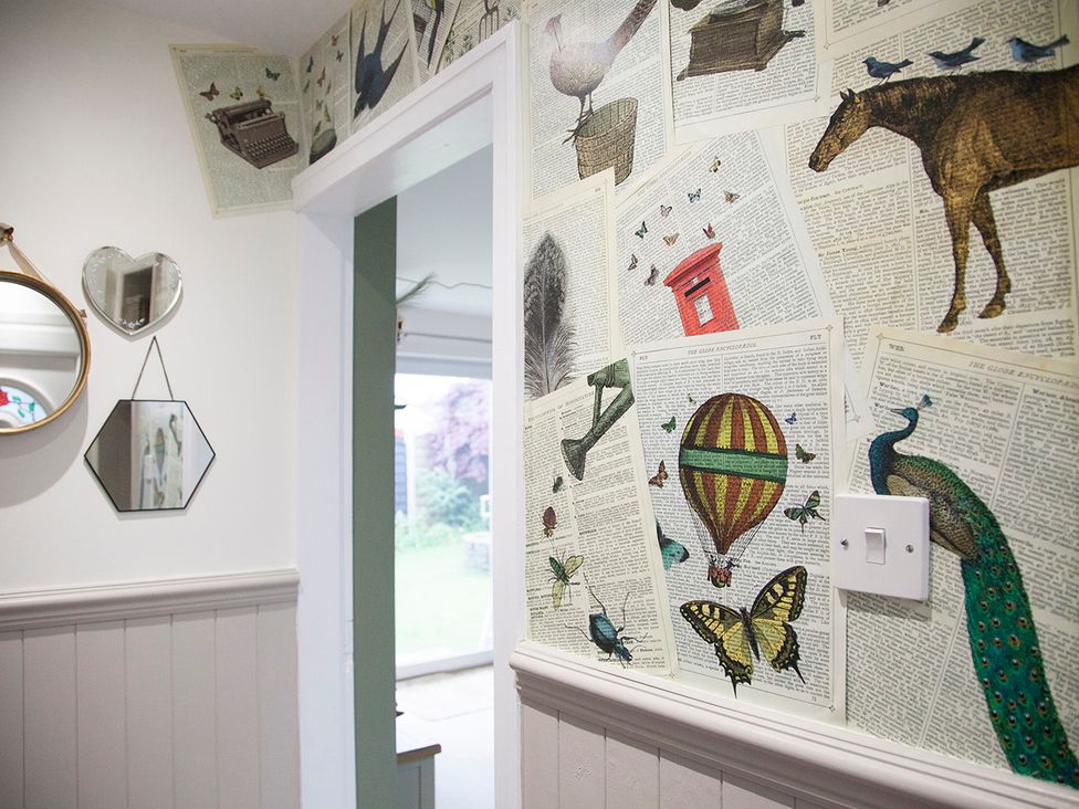 A hallway with decorative wall featuring illustrations and mirrors at Snug Cottage in Honley