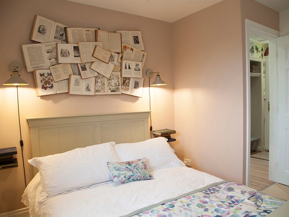 A bedroom with a bed and books displayed on the wall at Snug Cottage in Honley