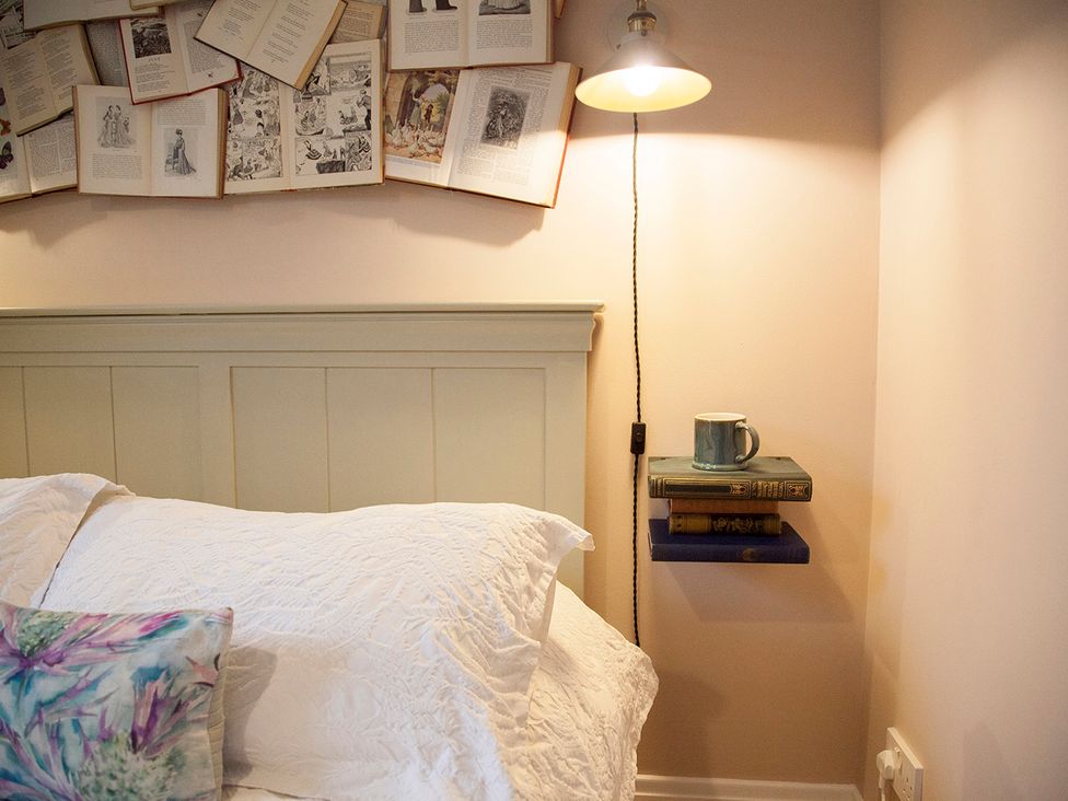 A bedroom with a bed and books on a shelf at Snug Cottage in Honley