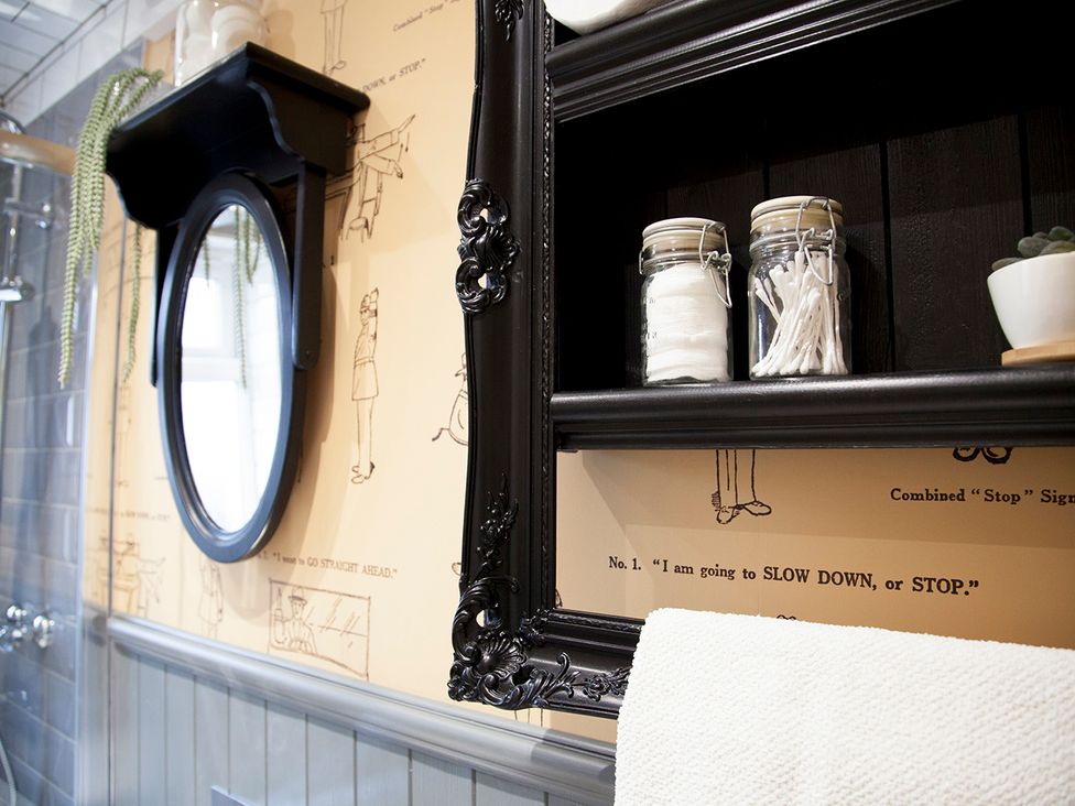 A bathroom with a mirror and shelf holding toiletries at Snug Cottage in Honley