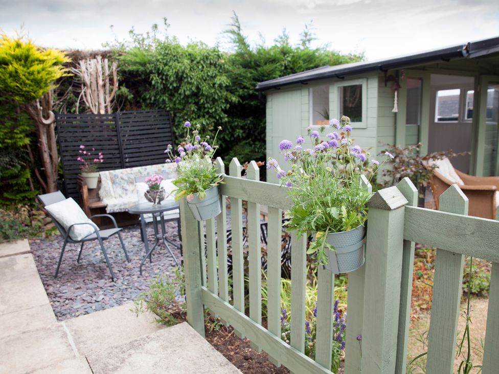 A garden with a fence, table, bench, and a shed at Snug Corner in Honley
