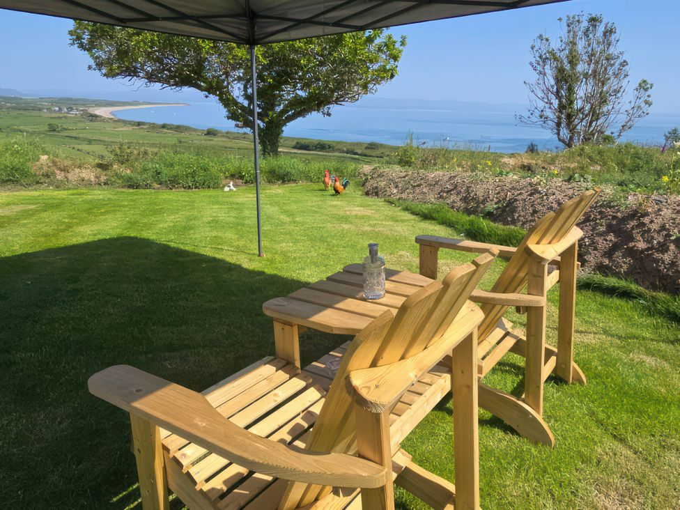 A garden with deck chairs and a table overlooking a landscape at Cwt Bugail Pwllheli