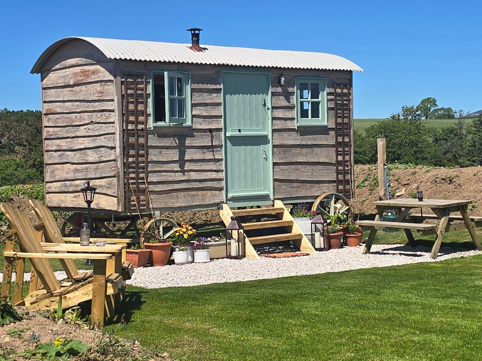 A wooden hut with steps and seating area at Cwt Bugail in Pwllheli