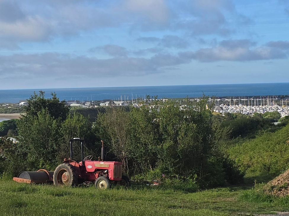 A tractor on grass with a view of the ocean and marina at Cwt Bugail in Pwllheli