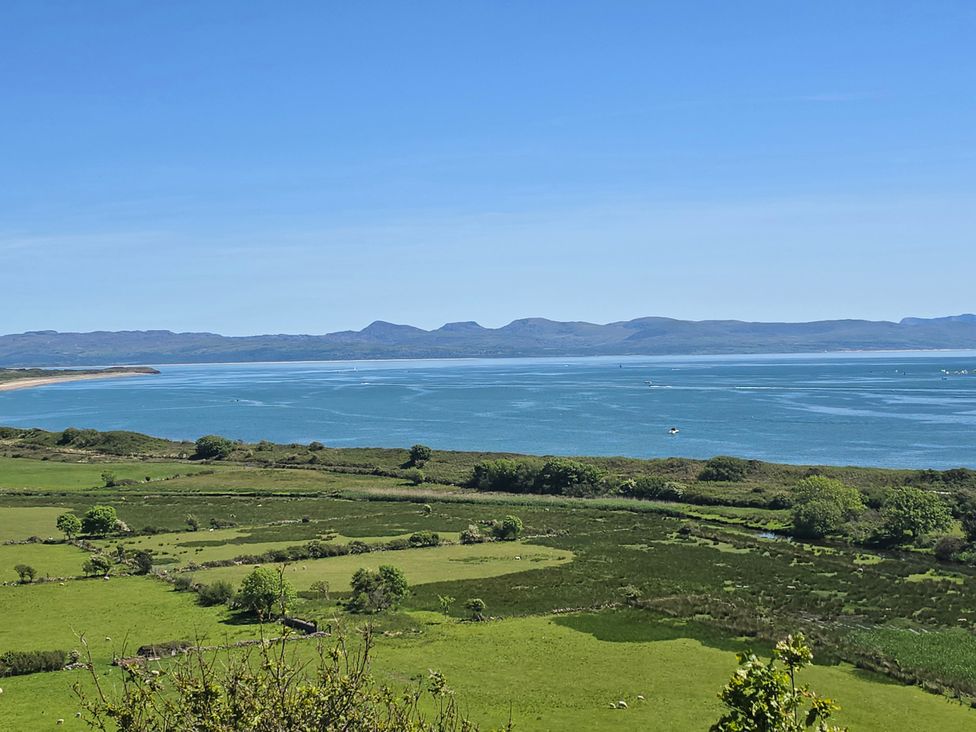 A view of water and hills with fields and boats at Cwt Bugail in Pwllheli