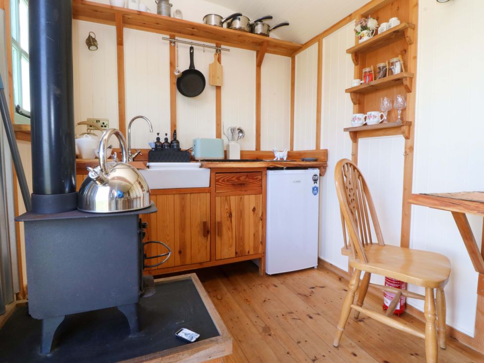 A kitchen with a stove, sink, and shelves at Cwt Bugail in Pwllheli