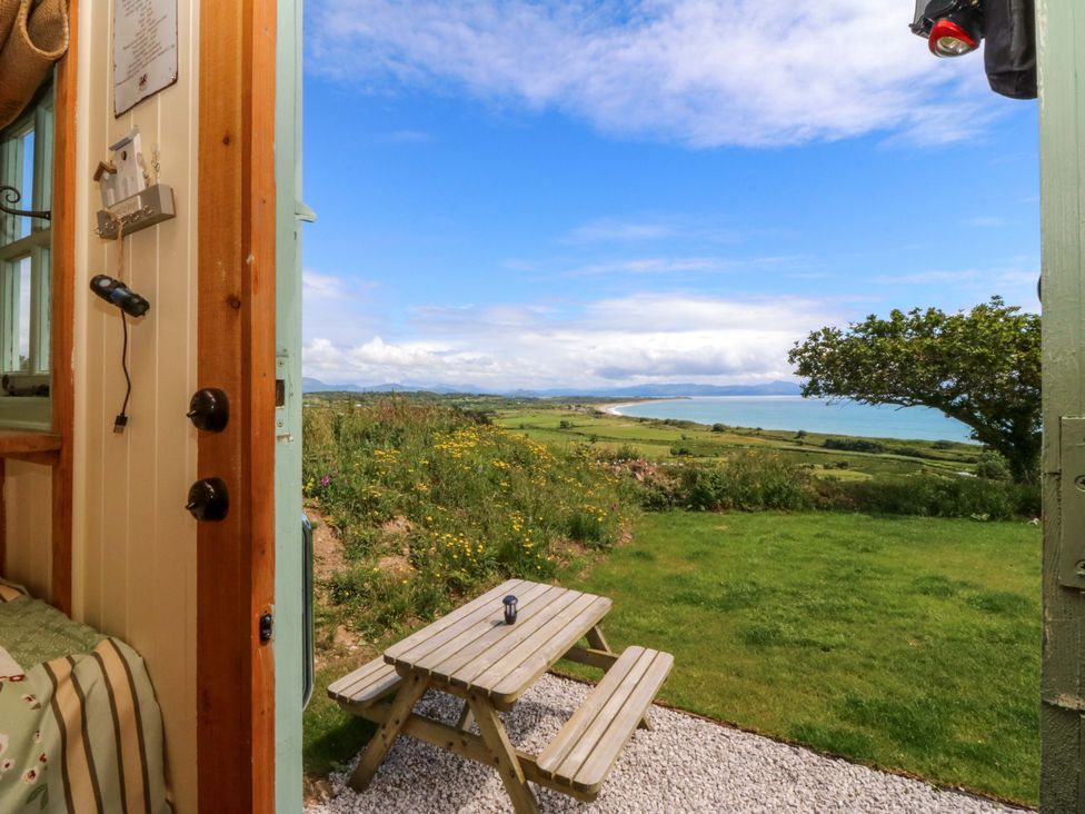 A view from a door looking at a table and chair in the garden at Cwt Bugail in Pwllheli