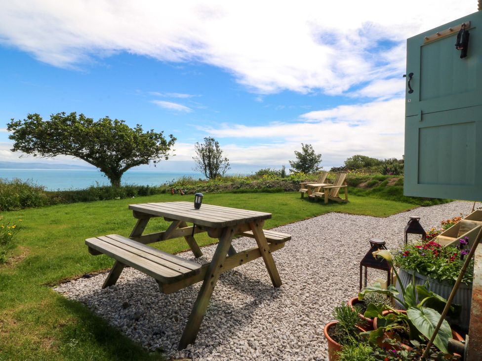 A picnic table on gravel with a view of the sea at Cwt Bugail Pwllheli