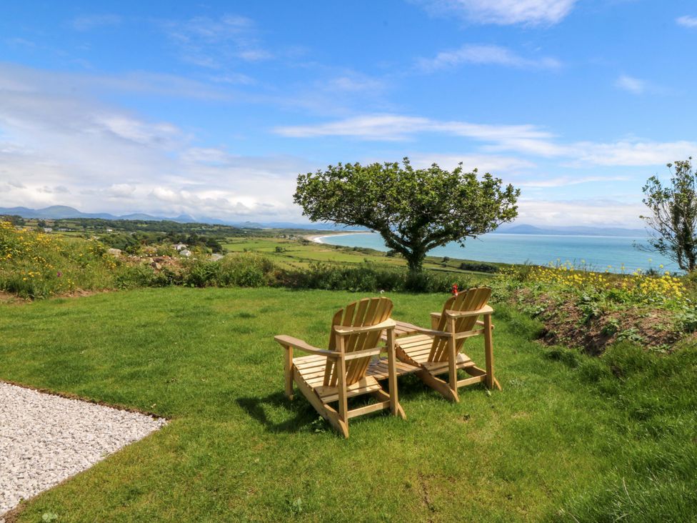 A garden with chairs and a view of the sea at Cwt Bugail in Pwllheli
