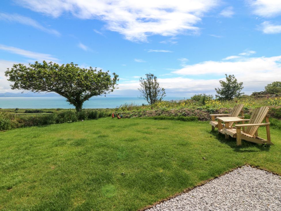 A garden with a tree and chairs overlooking the sea at Cwt Bugail in Pwllheli