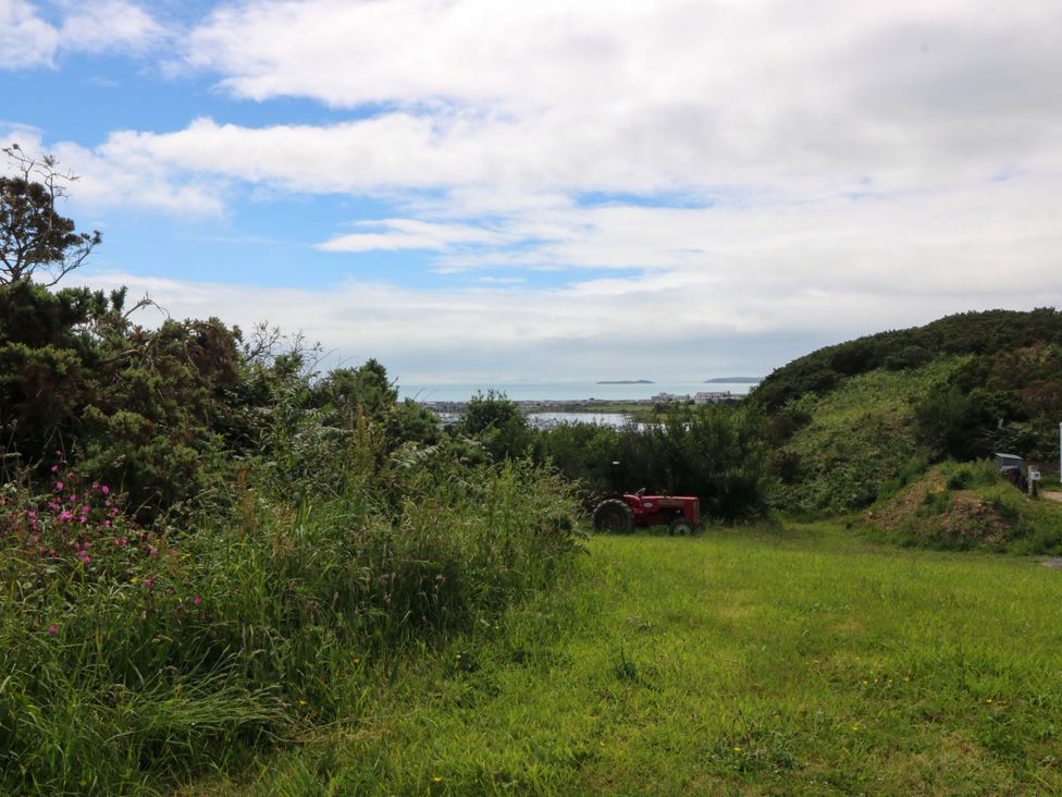 A grassy area with a tractor overlooking the ocean at Cwt Bugail Pwllheli