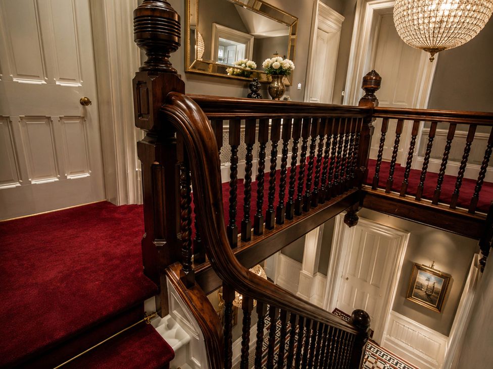 A staircase with a handrail and chandelier in a hallway at Chowdene Lodge Estate