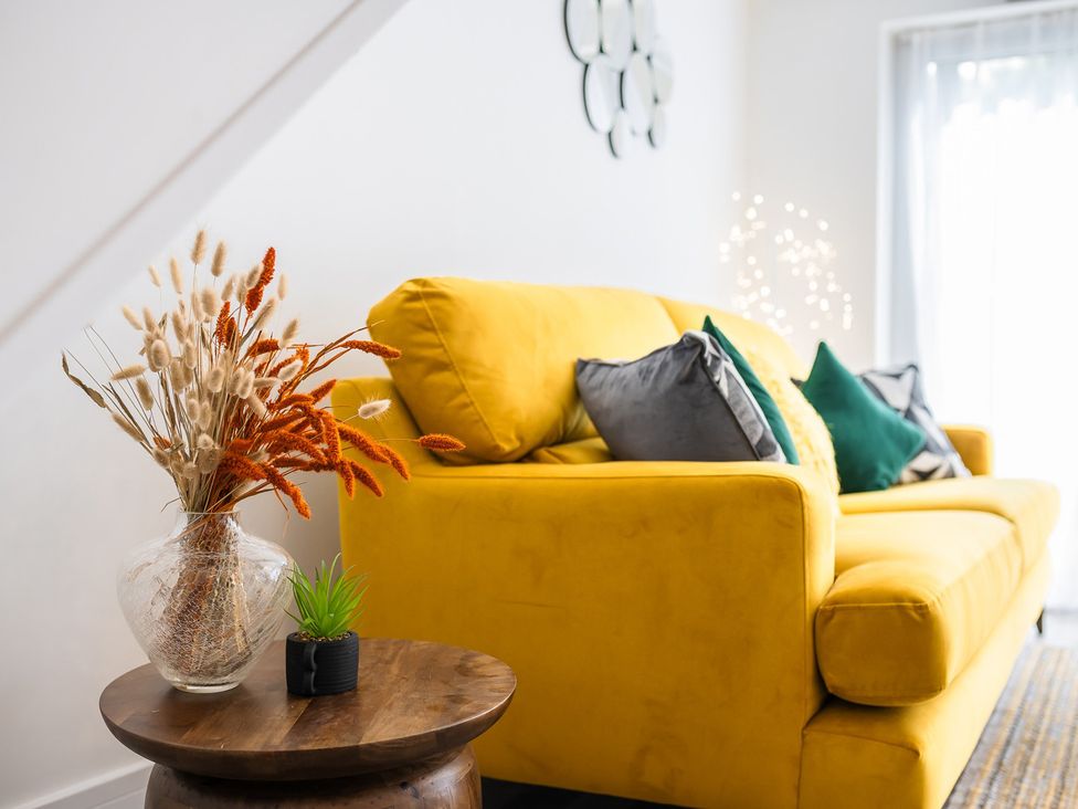 A living room with a yellow sofa and decorative plants at The Old Barn in Manchester