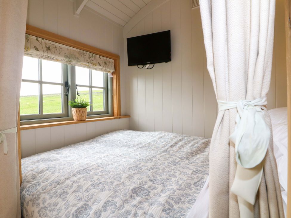 A bedroom with a bed, television and window at Pike House Farm Shepherds Hut 1 in Asbourne