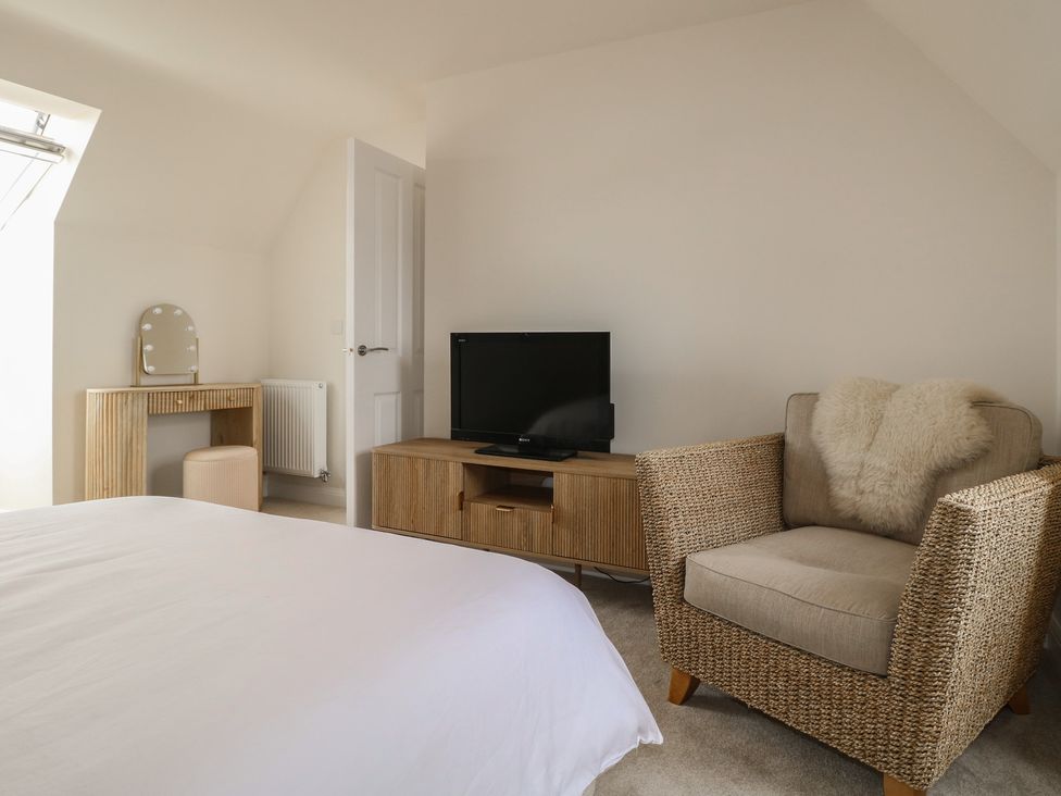 A bedroom with a bed, armchair, television, and dressing table at No.6 Beck Crescent in Ashbourne