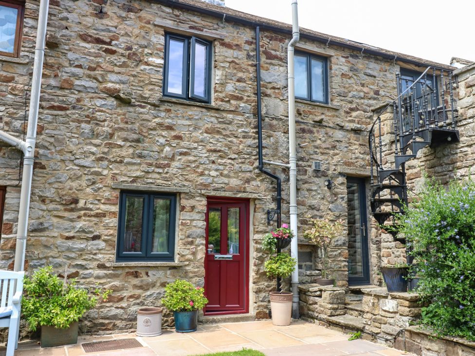 An outdoor view of a stone wall with a red door and windows at Kernot Cottage Reeth